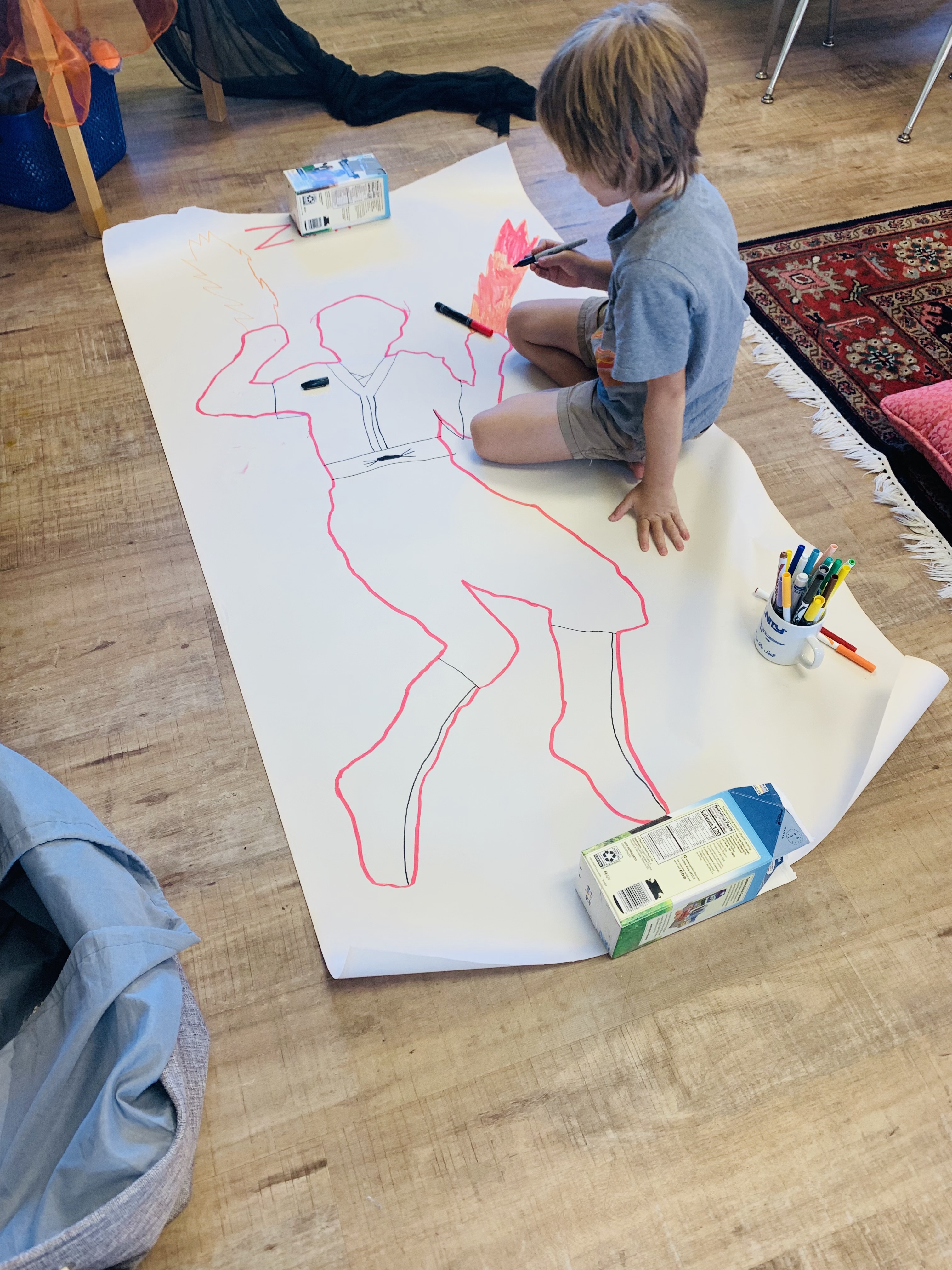A child coloring a large tracing of their body on a large piece of paper.